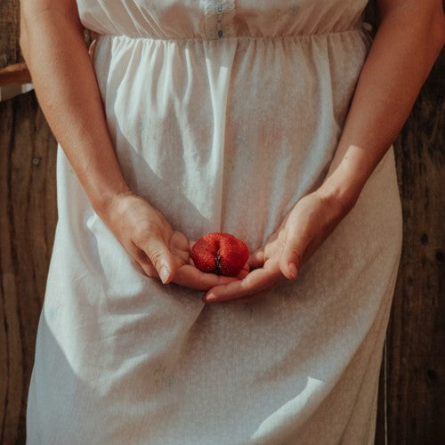 une femme tient une fraise avec ses de mains au niveau de son bas ventre