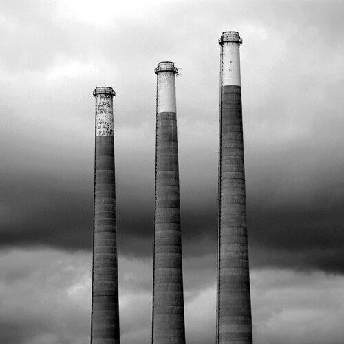 photo noir et blanc de trois cheminées d'usines qui polluent