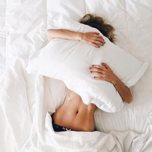 une femme allongée sur son lit sert son oreiller sur son visage