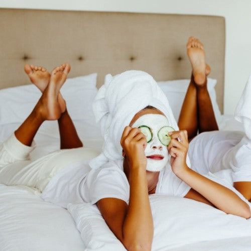 femme allongée sur son lit avec un masque sur le visage et des lamelles de concombre sur les yeux